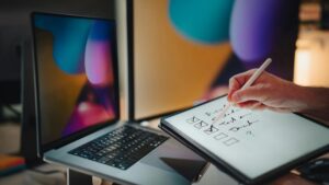 A hand using a stylus to check items off a digital checklist beside a laptop