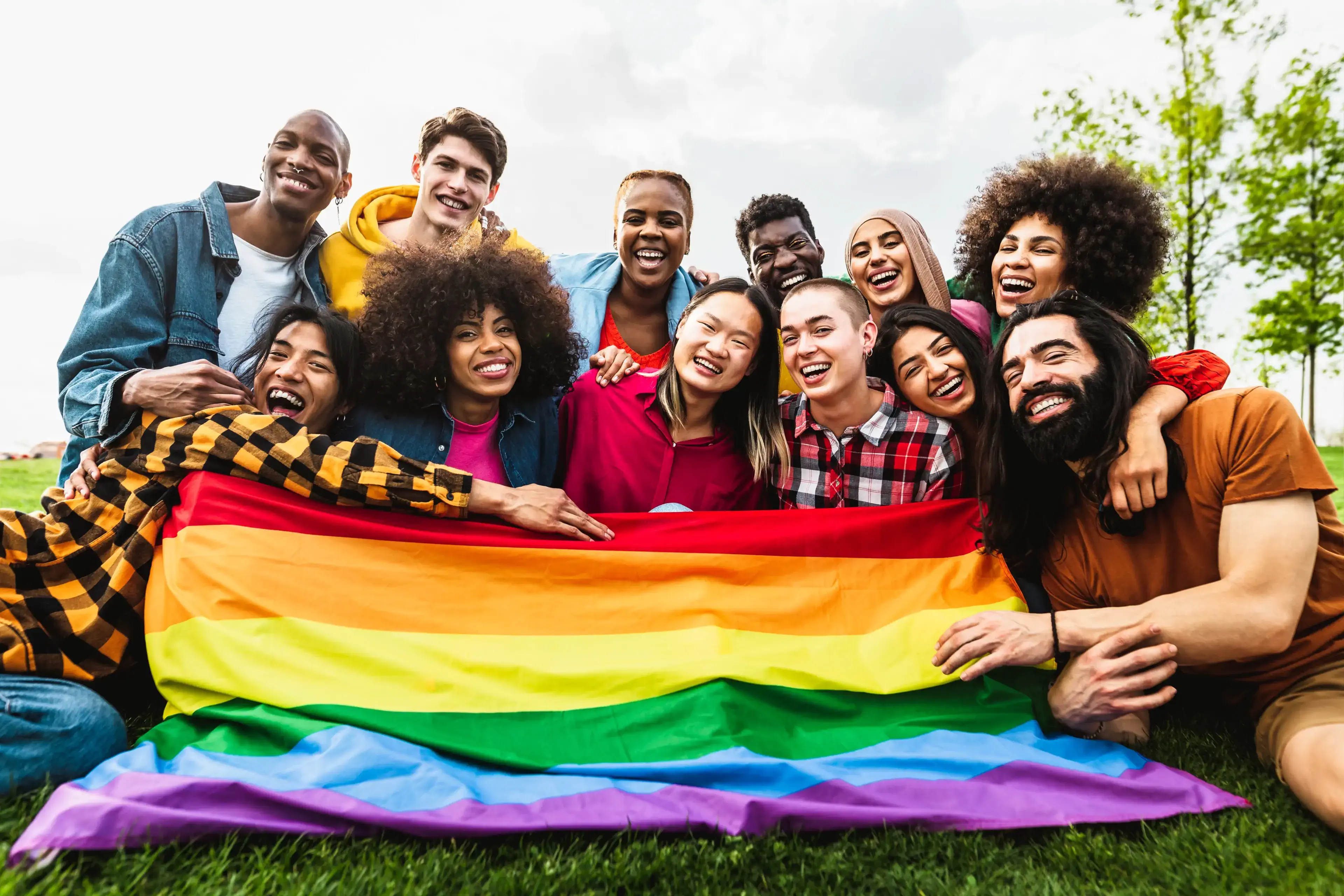 group of happy, diverse people holding a rainbow flag