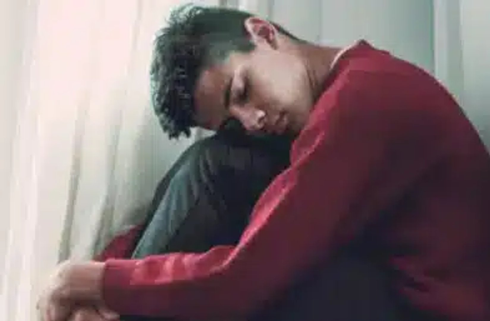 a teen boy with his head resting on his knees in sadness